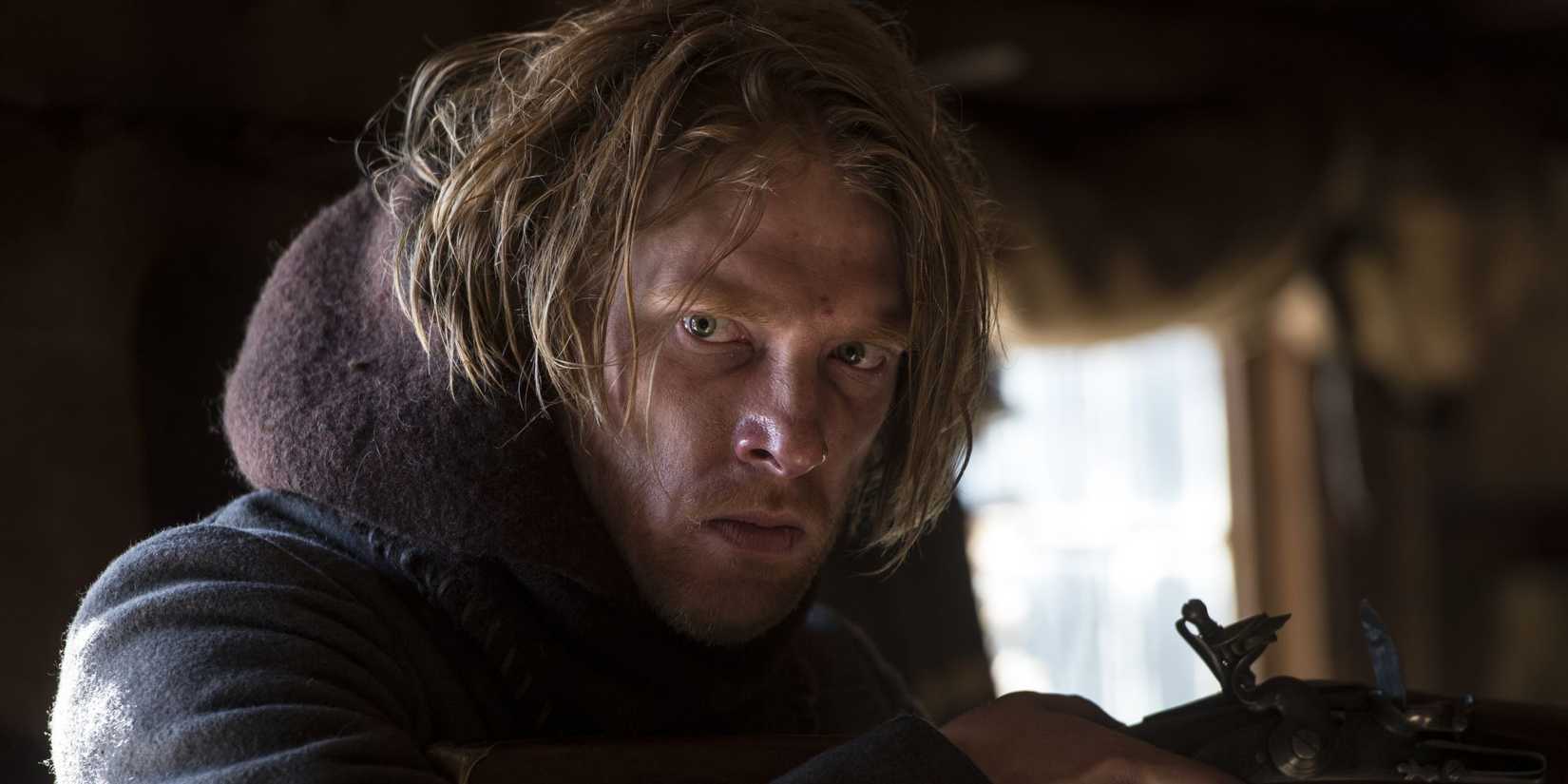 Domhnall Gleeson holding a rifle and looking serious in The Revenant.