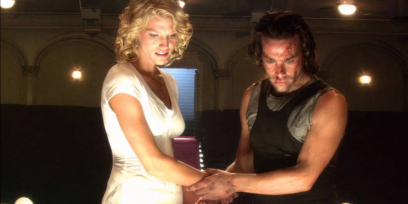 Tricia Helfer and James Callis with a wounded face look down at something in Battlestar Galactica.