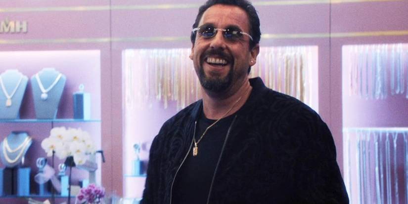 Adam Sandler wearing sunglasses in a jewelry store and smiling in Uncut Gems.