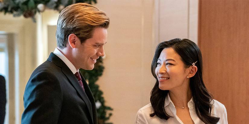Dominic Sherwood and Arden Cho smile at each other in an office hallway in Partner Track Season 1.