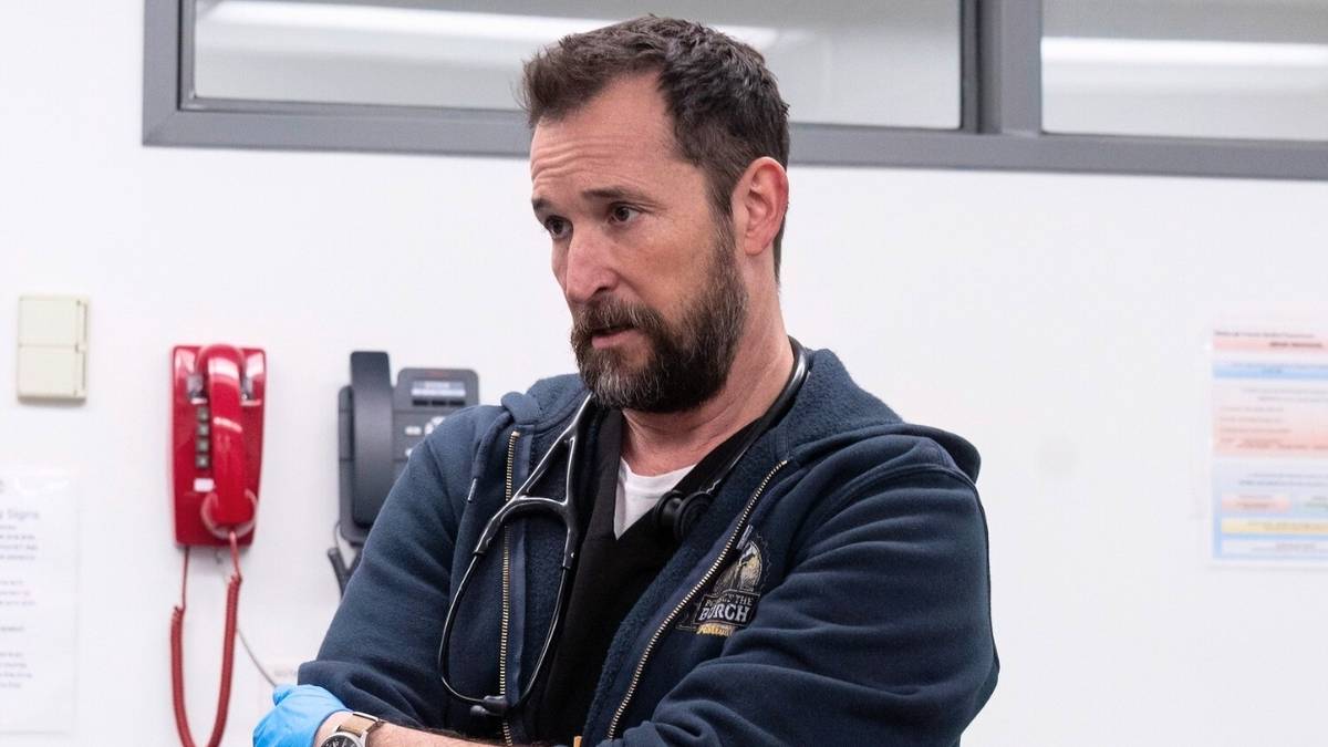 Noah Wyle standing with his arms crossed looking off-camera in The Pitt.