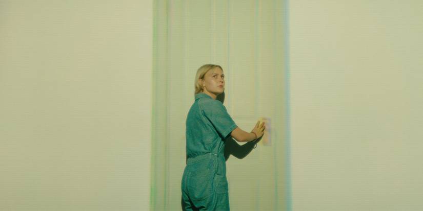 A person reaches out to touch a hallucination of a door on a blank wall in Wayward.