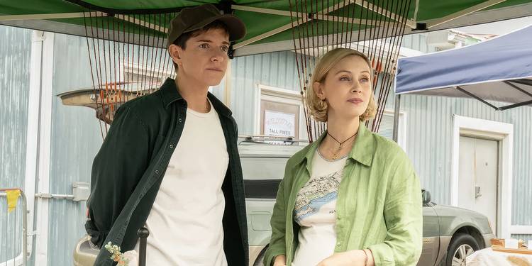 Mae Martin as Alex and Sarah Gadon as Laura standing under an awning and looking out in Wayward.