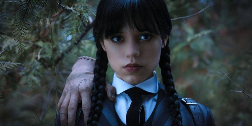 Jenna Ortega as Wednesday Addams with Thing on her shoulder outside by trees in Wednesday.