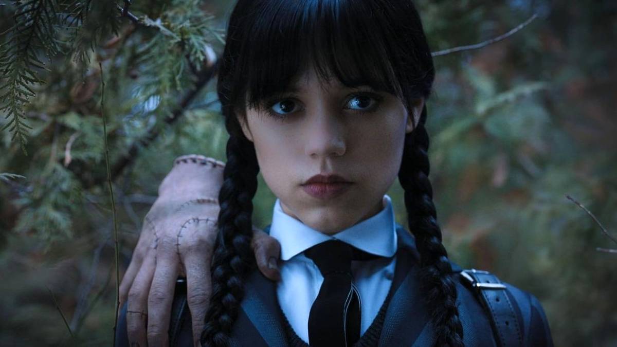 Jenna Ortega as Wednesday Addams with Thing on her shoulder outside by trees in Wednesday.