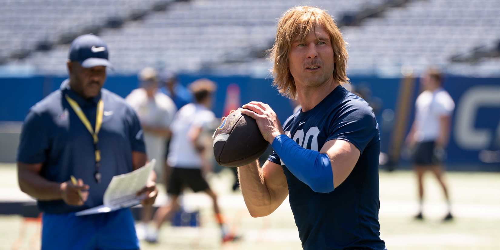 Glen Powell sebagai Chad Powers dengan kaos oblong dan melempar bola saat latihan di serial Hulu Chad Powers