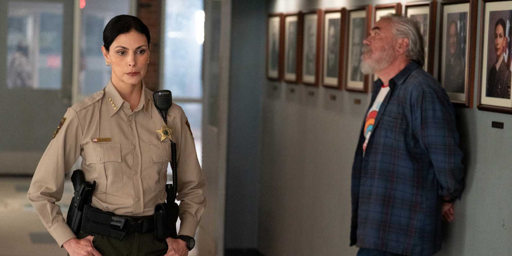 Morena Baccarin as Sheriff Mickey Fox passing W. Earl Brown as Wes down a hallway in Sheriff Country