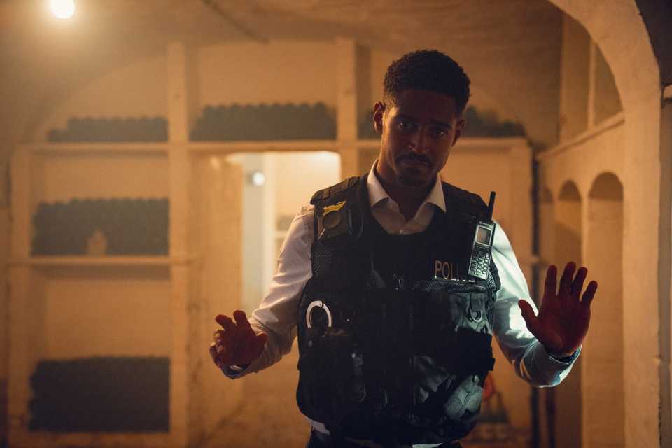 Alfred Enoch in his police uniform holding up his hands in Run Away