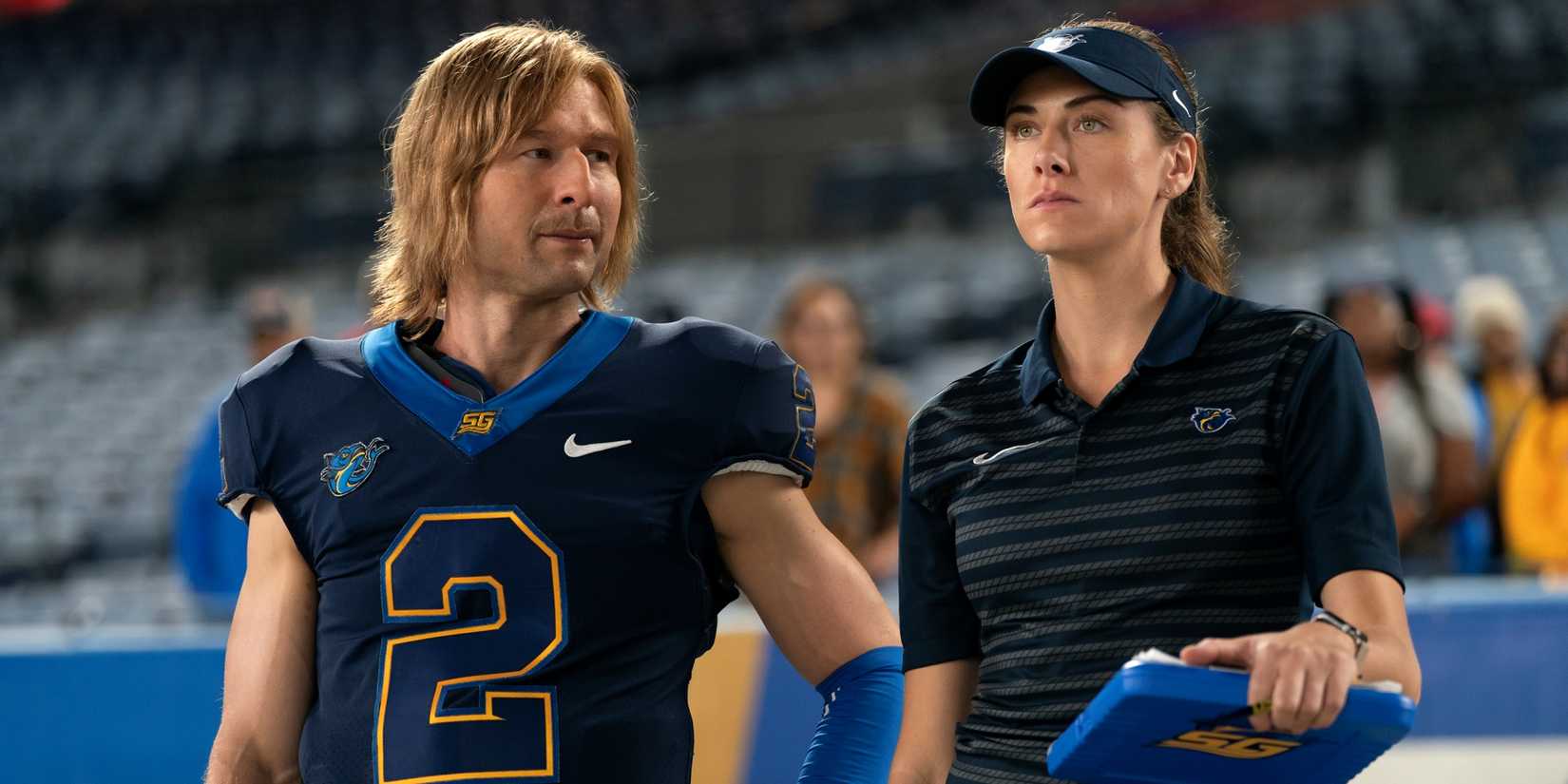 Glen Powell as Chad Powers standing next to and looking at Perry Mattfeld as Ricky Hudson in Chad Powers