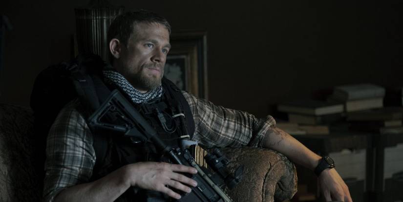 Charlie Hunnam holding a gun and sitting down in Triple Frontier.