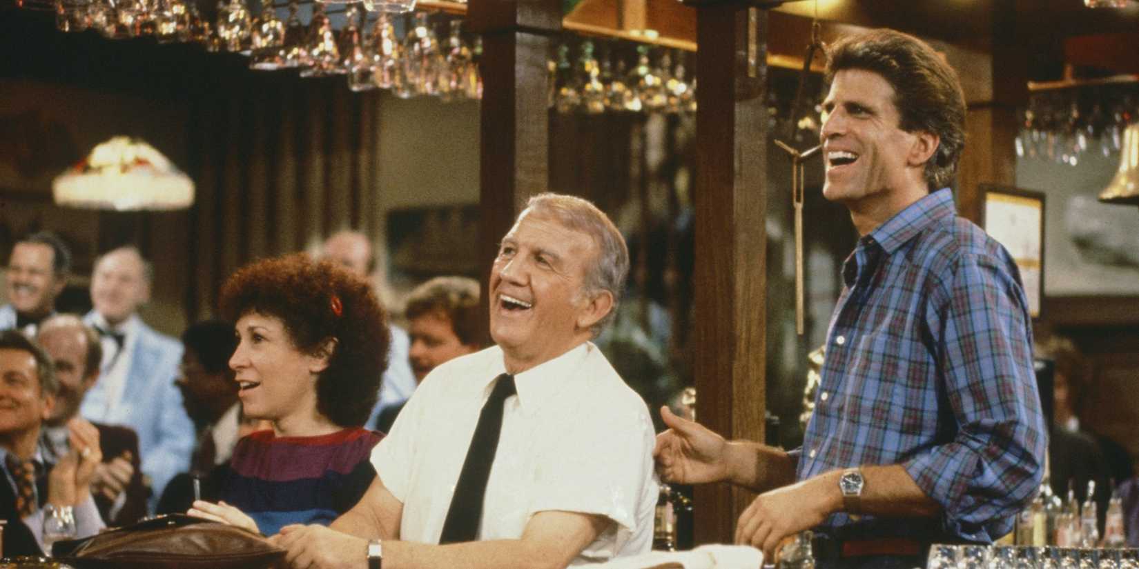 Carla, Coach, and Sam behind the bar laughing in the pilot episode of Cheers