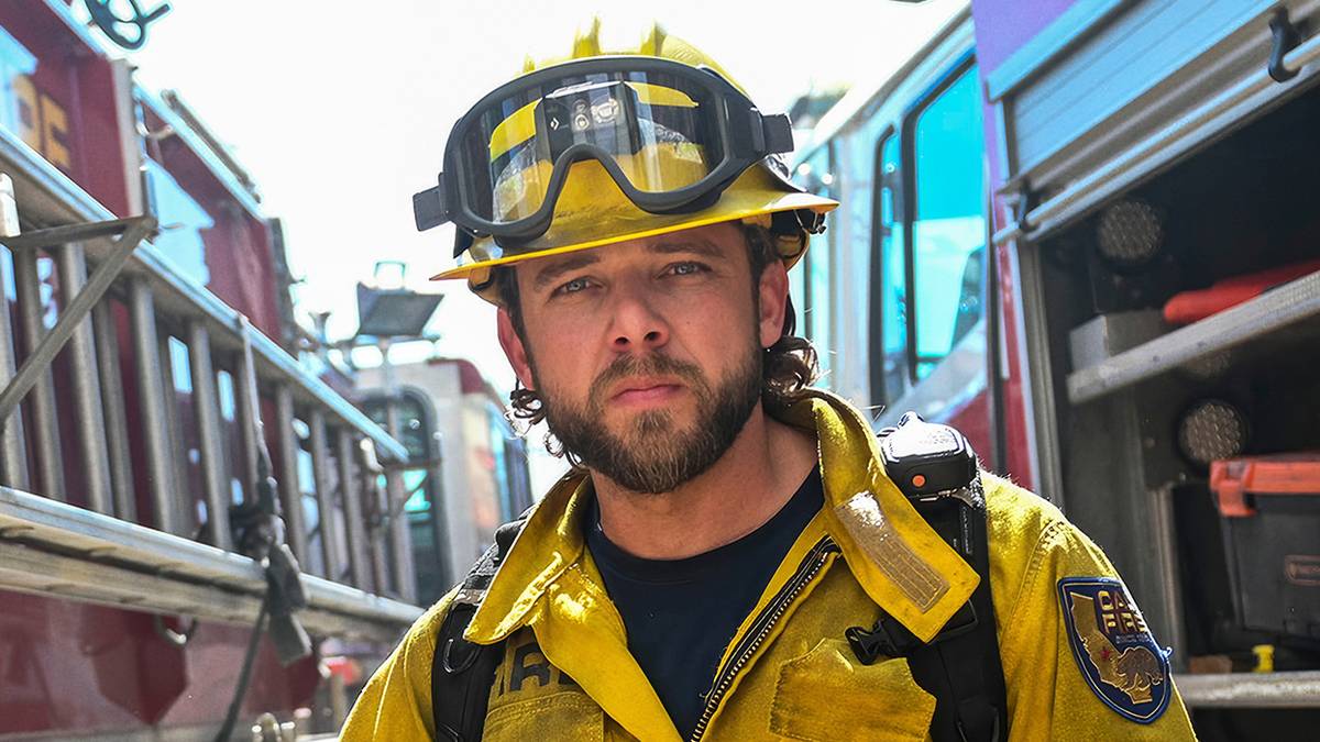 Max Thieriot as Bode Leone standing in between two fire trucks in his fire gear in Fire Country Season 4