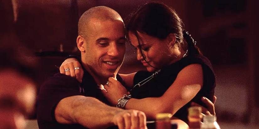 Letty sits in Dom's lap as they smile together in The Fast and The Furious, 2001.
