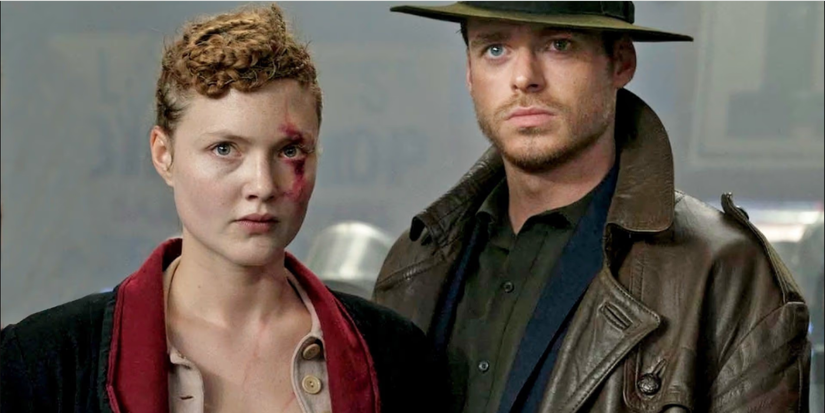 A woman with a marking on her face stands next to a man wearing a hat and leather jacket in Electric Dreams.