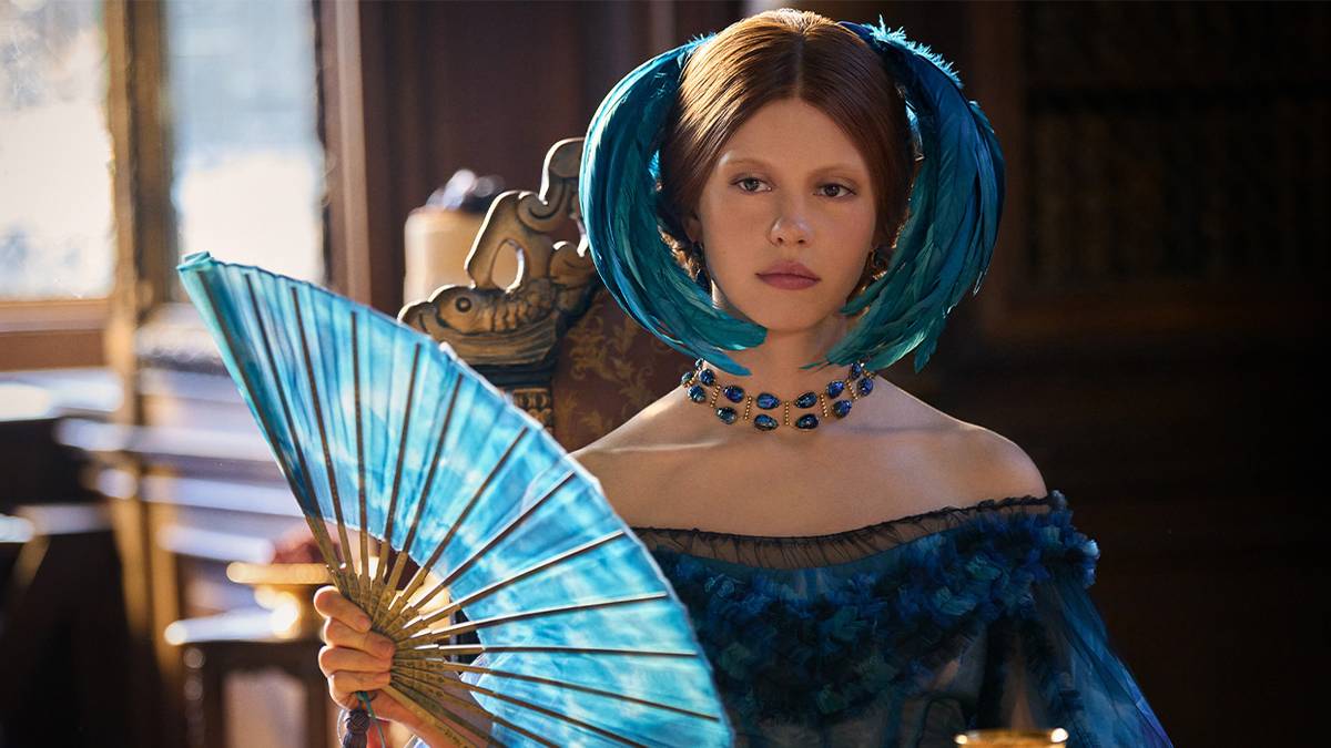Elizabeth (Mia Goth) in a blue dress with blue feathers in her hair, holding a blue fan in 'Frankenstein' (2025)