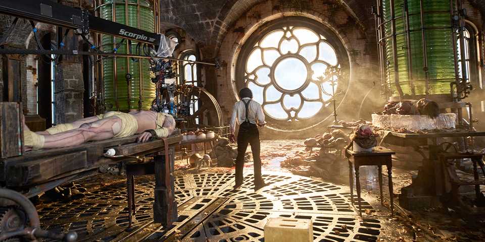 Victor stands in front of a window with sunlight coming through, the Creature on a table behind him in the lab.