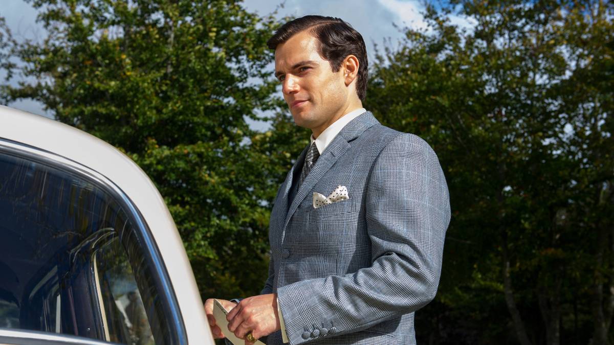 Henry Cavill as Solo smiling near a parked car in The Man from UNCLE