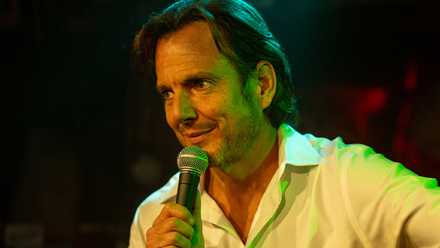 Will Arnett as Alex Novak, holding a microphone in Is This Thing On?