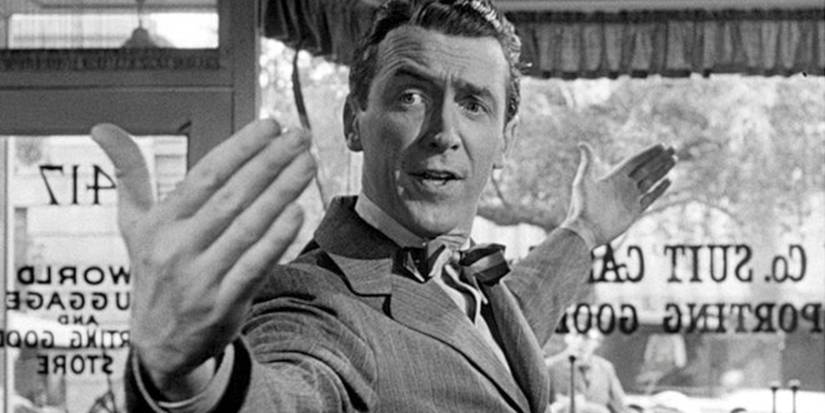 James Stewart as George Bailey motions he wants a big suitcase, standing in a store in It's a Wonderful Life.