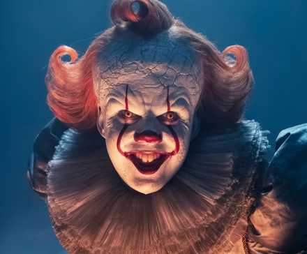 Bill Skarsgard as Pennywise bending over and smiling for the camera in It: Welcome to Derry