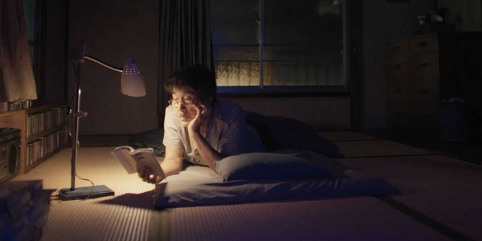 Kōji Yakusho as Hirayama in Perfect Days lying on the floor reading