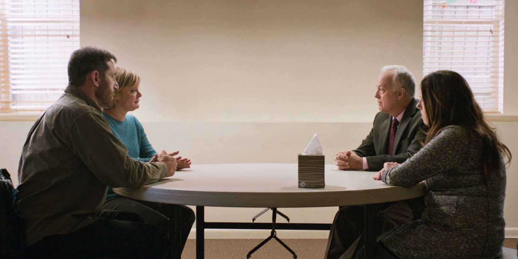 Jason Isaacs, Martha Plimpton, Ann Dowd, and Reed Birney sit at a small table and talk in Mass.