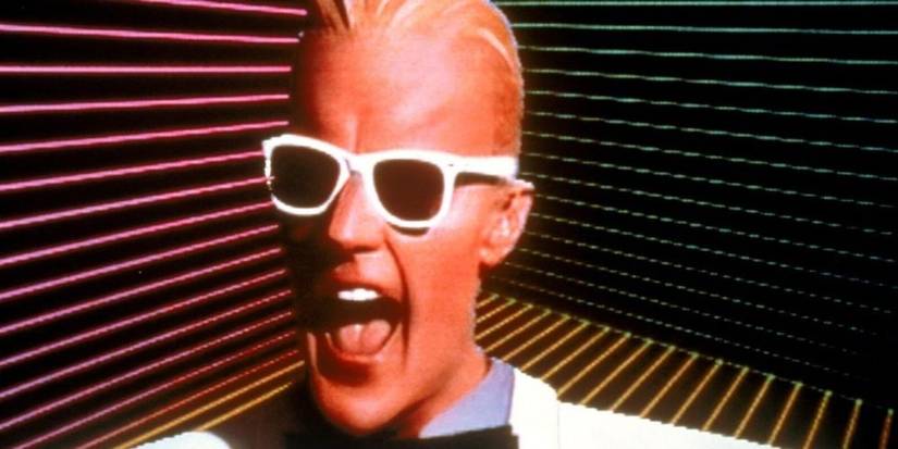 Matt Frewer as Max Headroom with sunglasses in front of a digital striped background. 