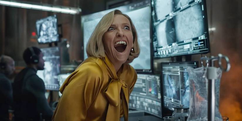 Toni Collette with her mouth wide in excitement, sitting in front of monitors, in Mickey 17