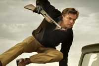Leonardo DiCaprio as Rick Dalton jumping over a car with a gun in Once Upon a Time... in Hollywood.
