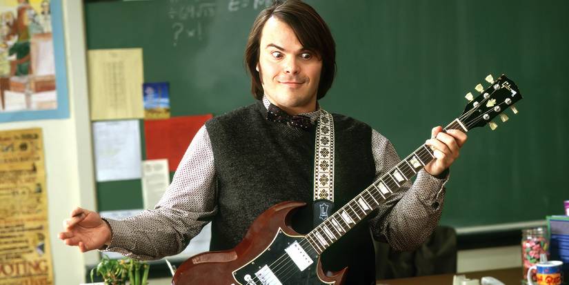Jack Black with wide eyes holding a guitar in the front of a classroom in School of Rock.