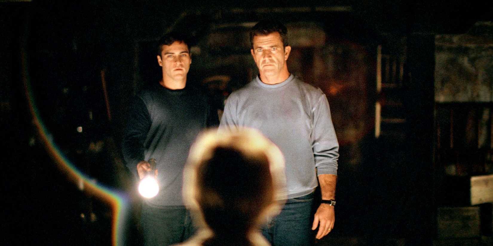 Mel Gibson and Joaquin Phoenix shine a flashlight on a small figure and look tense in Signs.