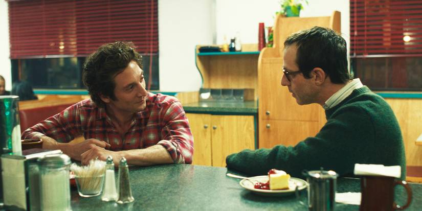 Young Bruce Springsteen sitting at a diner counter smiling at producer Jon Landau.