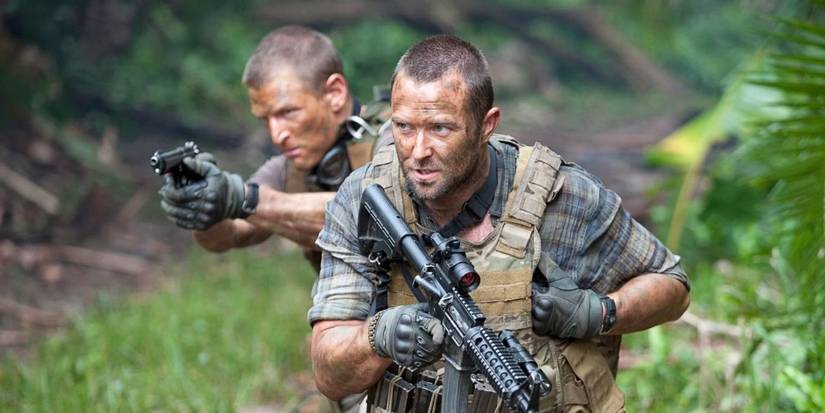Two men in camouflage fatigues walk through a jungle and hold weapons in Strike Back.
