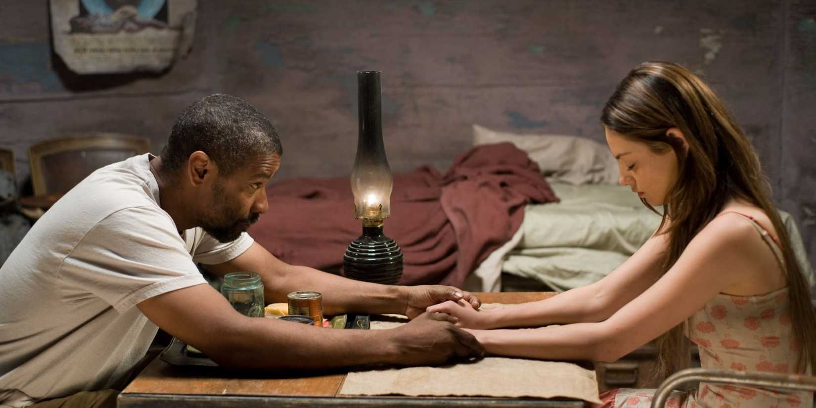 Denzel Washington as Eli holds hands across a table saying grace with Mila Kunis as Solara in The Book of Eli.