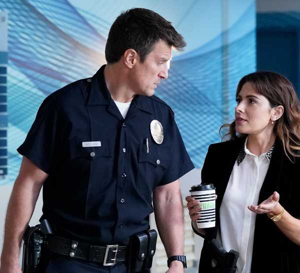 Jessica Russo (Sarah Shahi) chats with John Nolan (Nathan Fillion) as they walk down a hall in The Rookie.