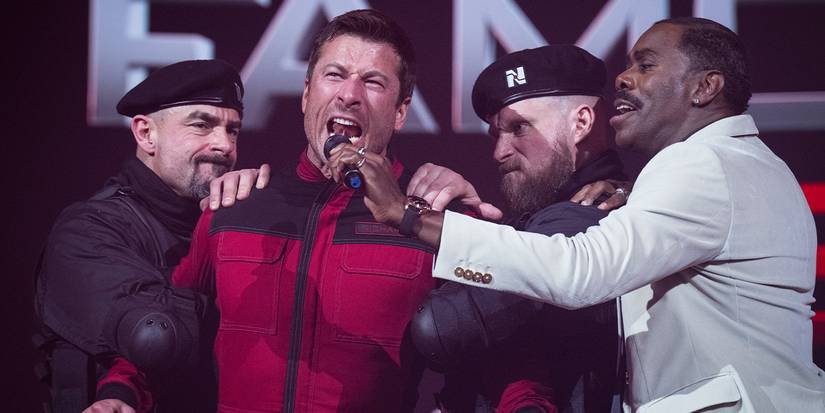 Bobby Thompson holds a microphone up to a screaming Ben Richards, who's being restrained by guards.