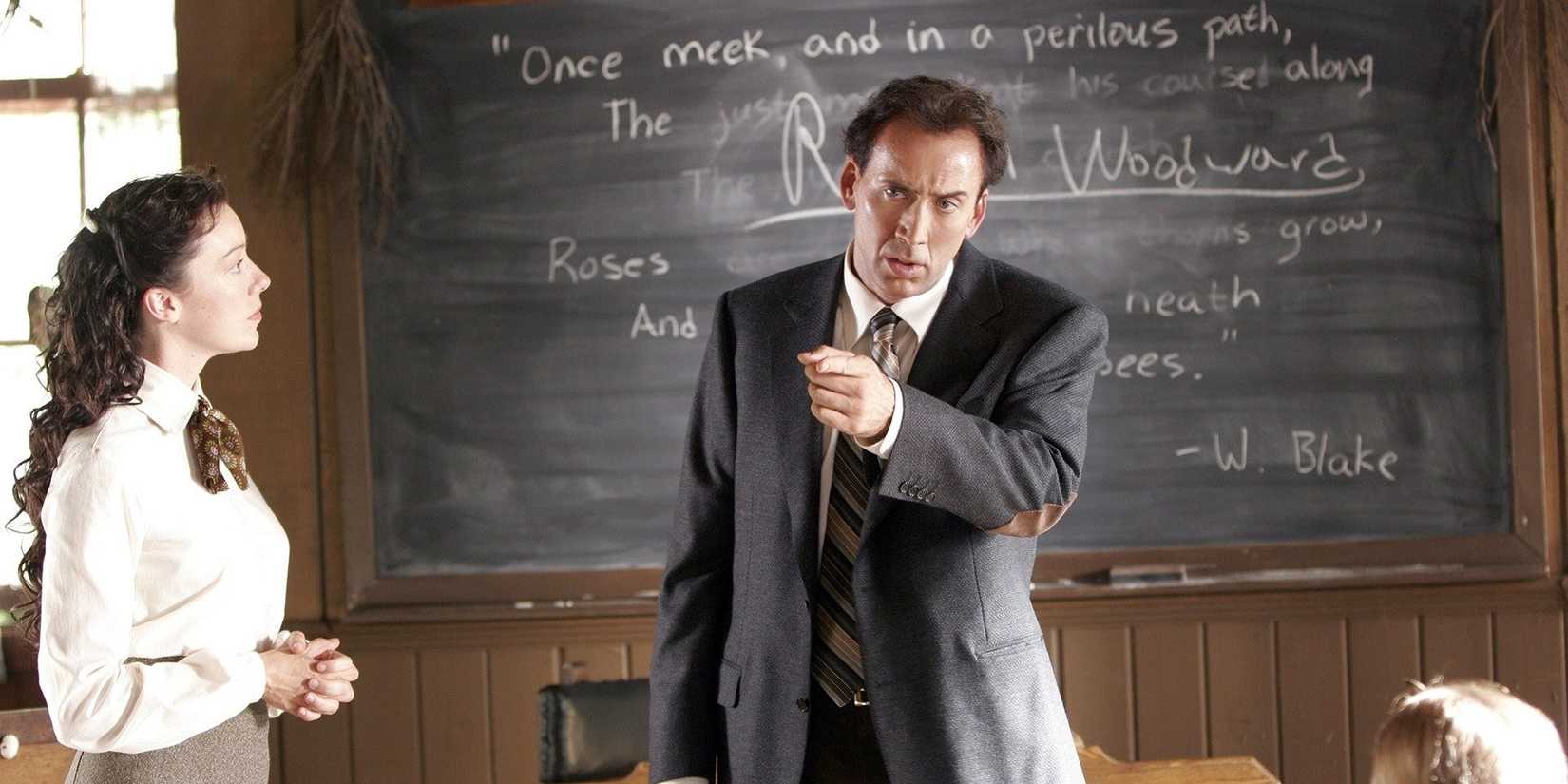 Nicolas Cage as Edward Malus stands in front of a blackboard pointing at something while Molly Parker as Sister Rose watches him in The Wicker Man