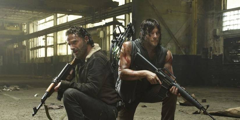 Andrew Lincoln sebagai Rick dan Norman Reedus sebagai Daryl berjongkok di sebuah gedung dengan senjata besar di The Walking Dead.