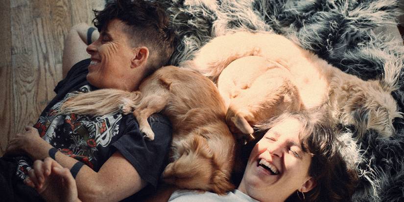 Andrea Gibson and Megan Falley laughing and laying with their dog in Come See Me in the Good Light