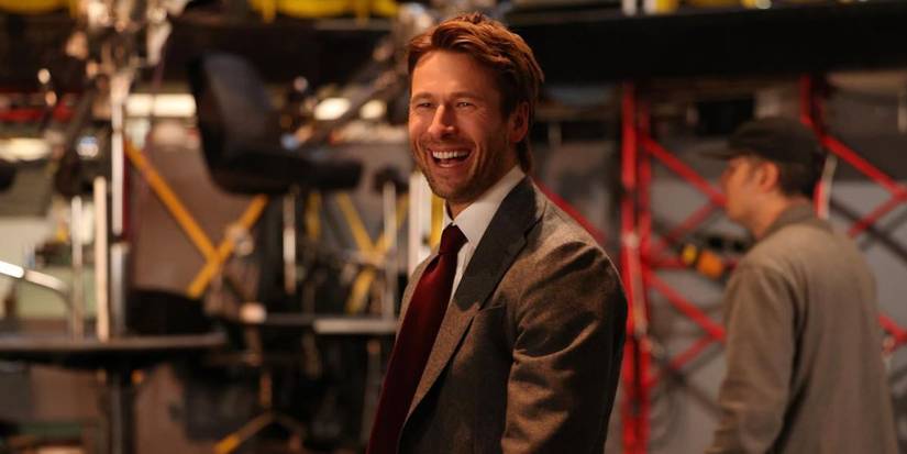 Glen Powell grinning in a brown suit in a promo for SNL, Season 51, Episode 6.