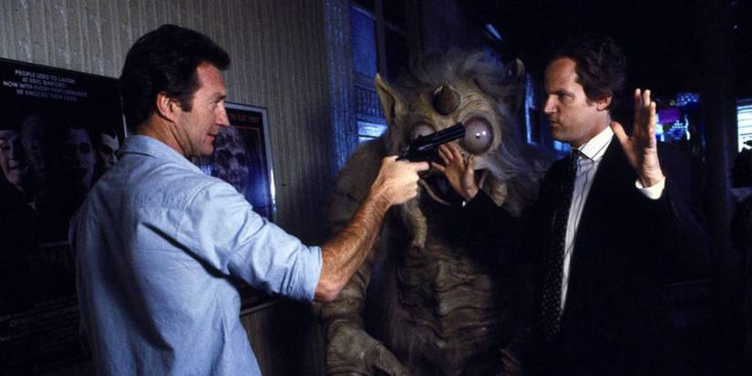 Rollie (Bryan Brown) points a gun at a man