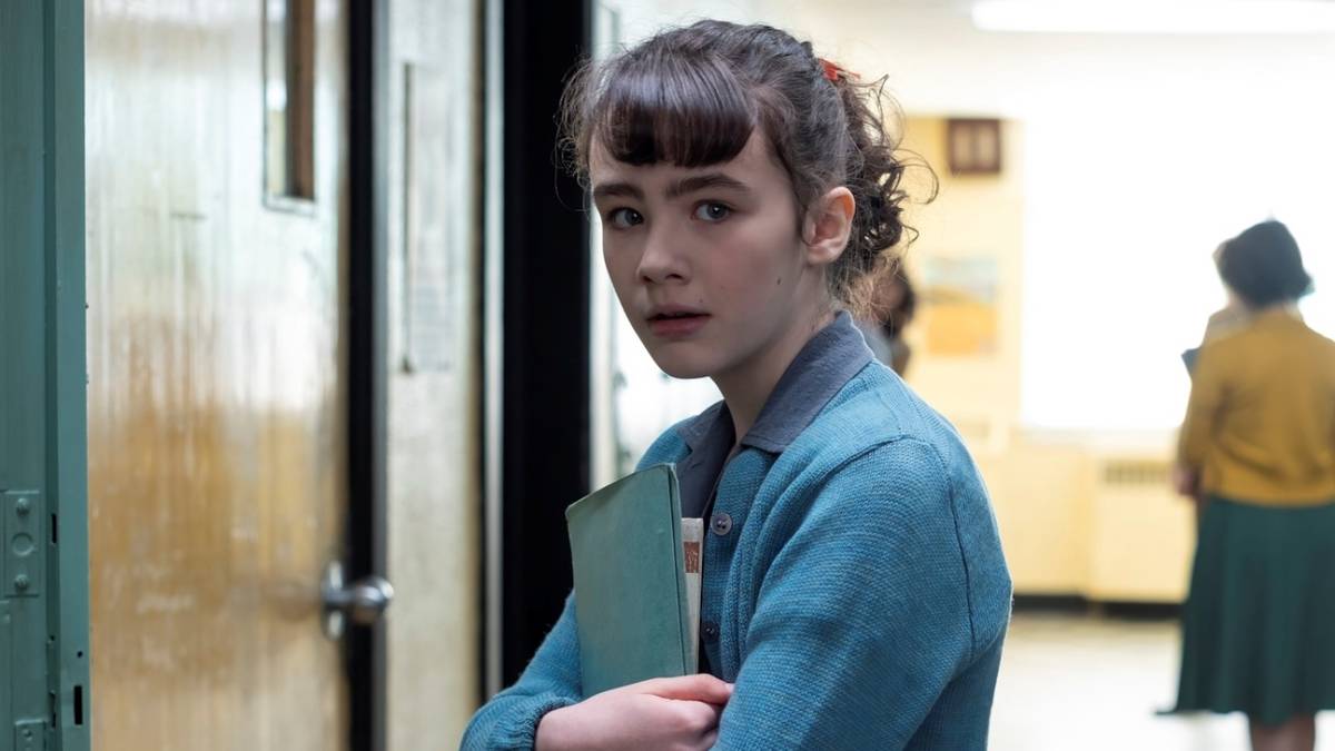 Clara Stack as Lilly Bainbridge holding her books to her chest at her school locker in IT: Welcome to Derry