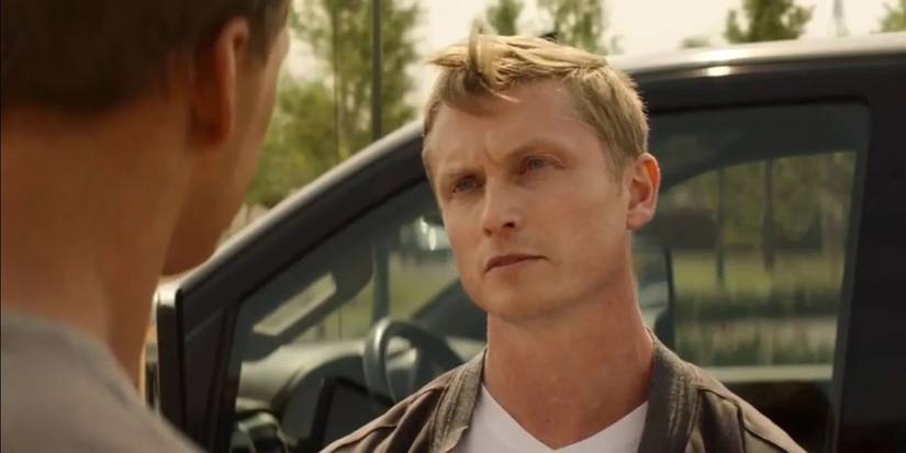 Chris Webster sebagai Kliner Jr. berbicara dengan seseorang di luar kendaraan di Reacher.