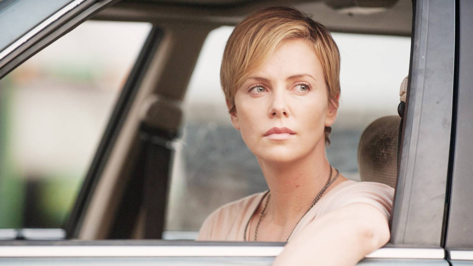 Charlize Theron sits in the drivers seat of a car with the window rolled down in Dark Places
