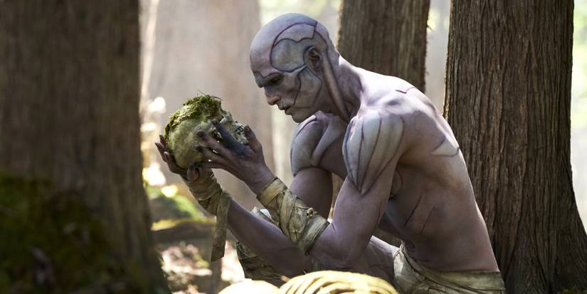 Jacob Elordi as the Creature examines a moss-covered skull in the woods in Guillermo del Toro's Frankenstein
