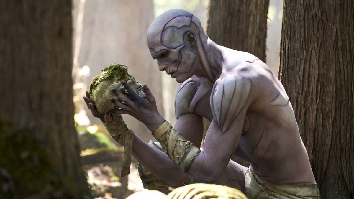 Jacob Elordi as the Creature examines a moss-covered skull in the woods in Guillermo del Toro's Frankenstein