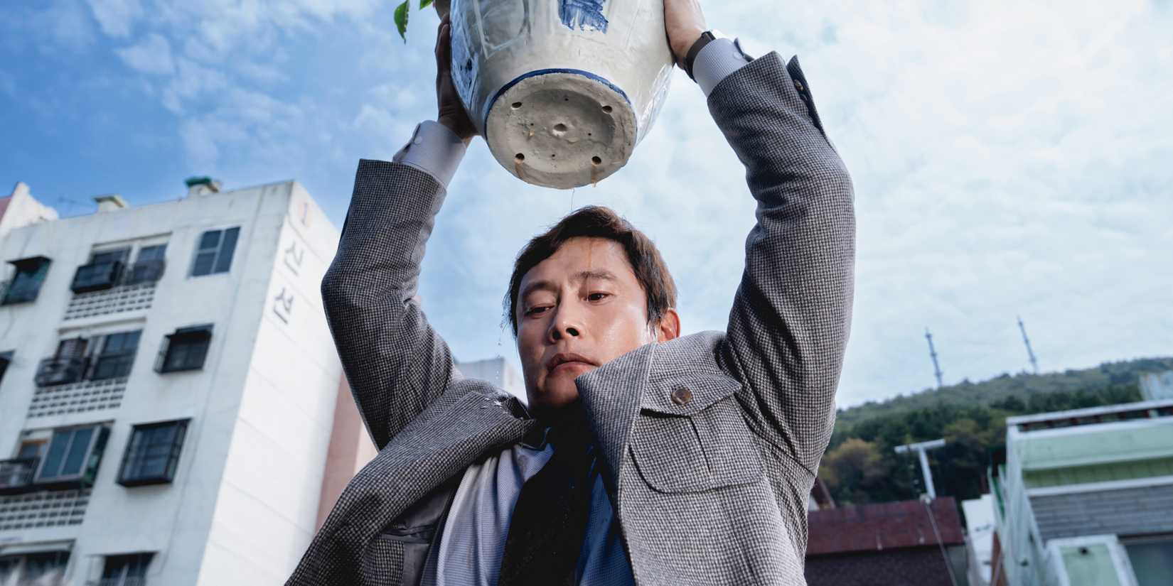 Lee Byung-hun raising a flowerpot in No Other Choice