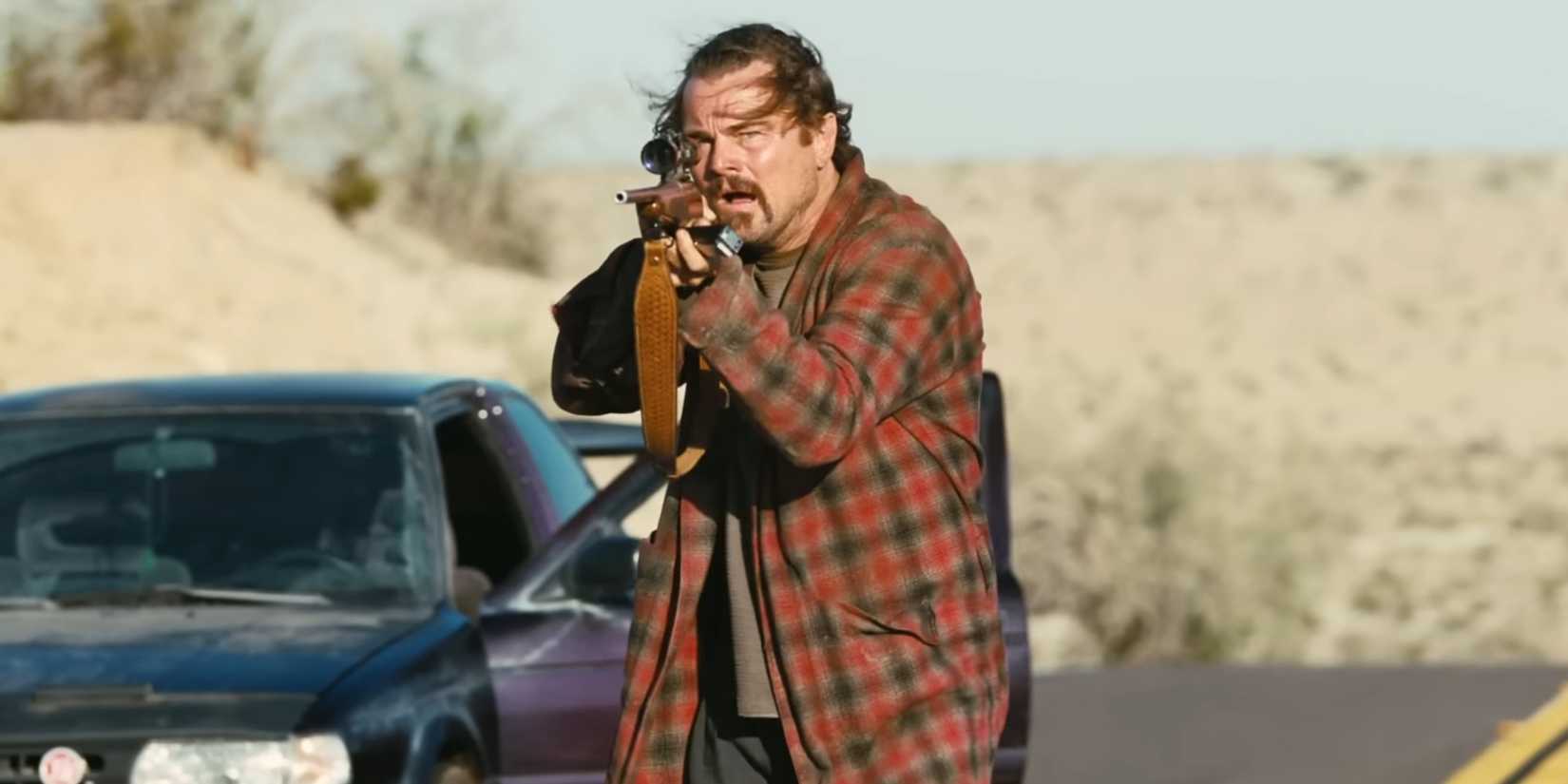 One Battle After Another - Leonardo DiCaprio aims a weapon while walking near his stopped car