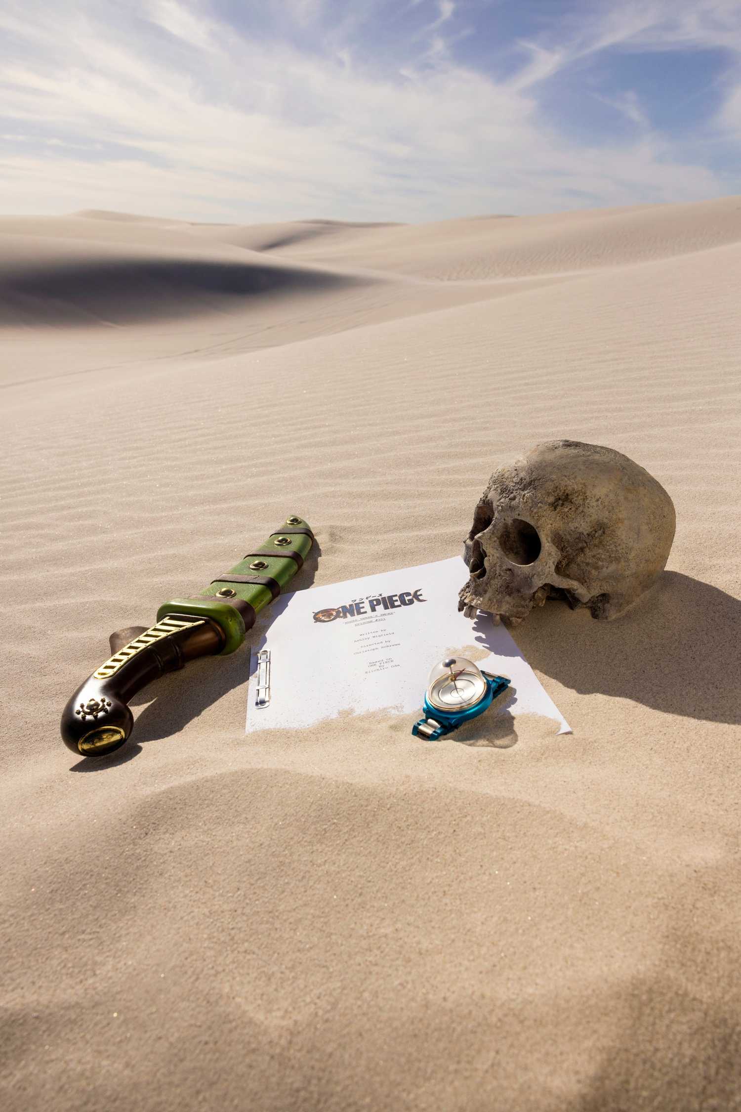 A poster featuring a dagger, compass, skull and script in the desert for the star of One Piece Season 3's production