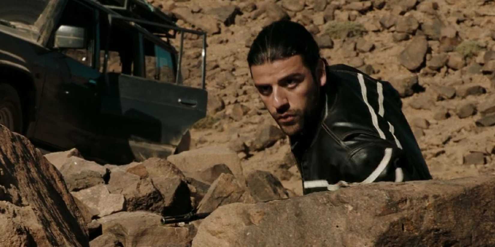 Oscar Isaac crouching down behind rocks and looking ahead in Body of Lies.